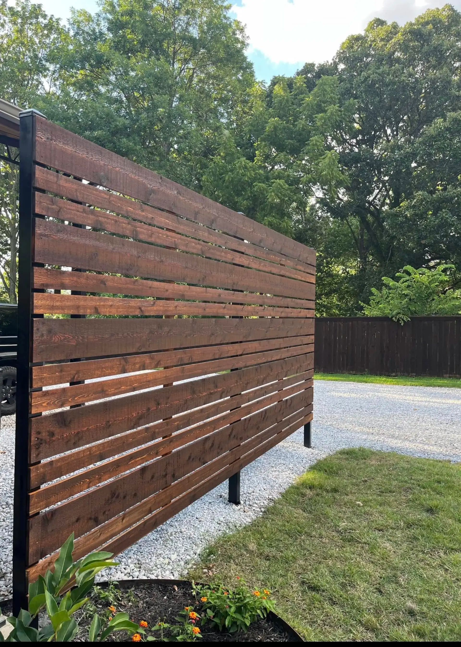 Cedar privacy screen with a horizontal picket design and 1-inch gaps for airflow, built around a carport adjoining a patio. Stained dark brown.