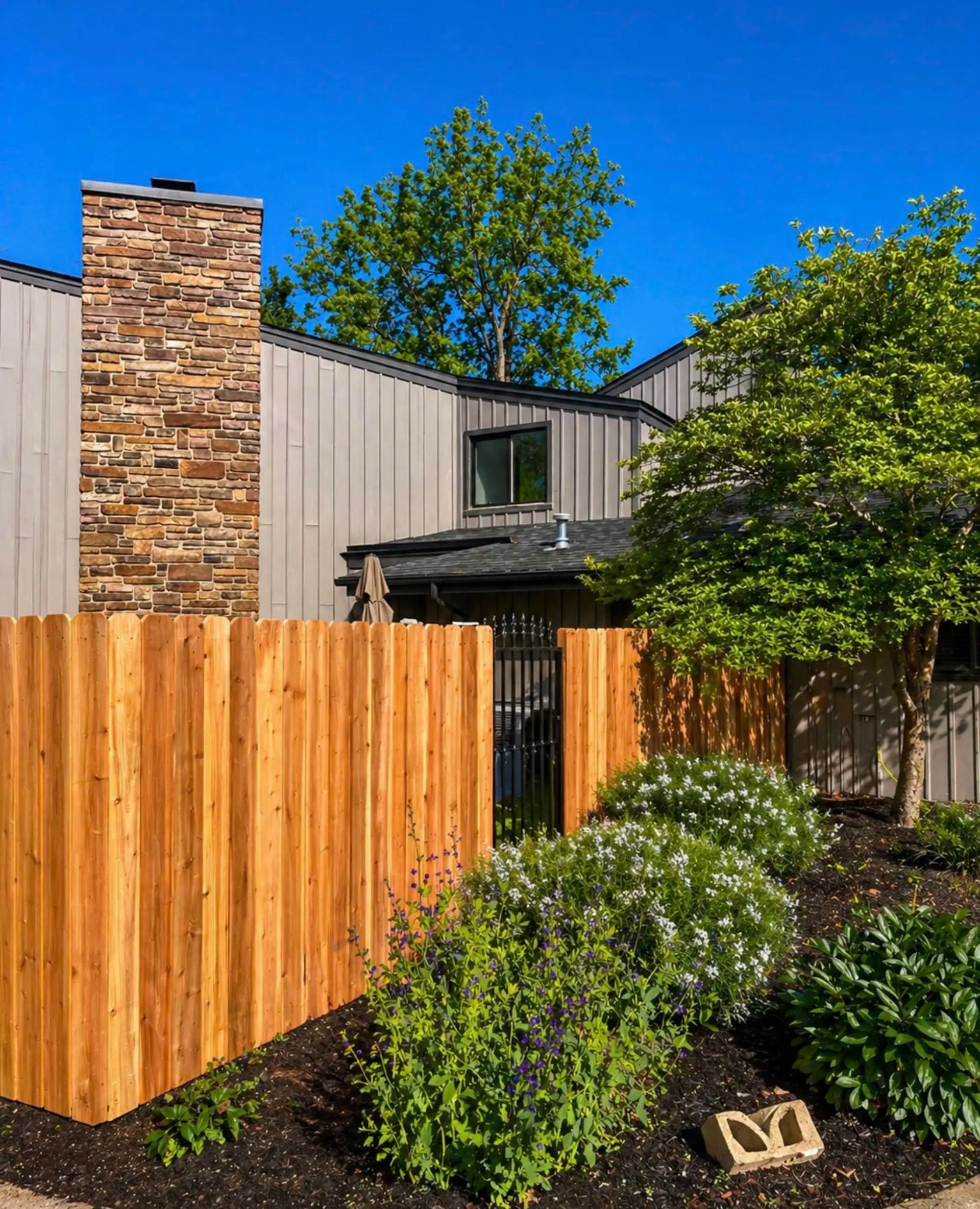 Traditional cedar fence around an older home with professional landscaping, featuring an ornamental metal gate.